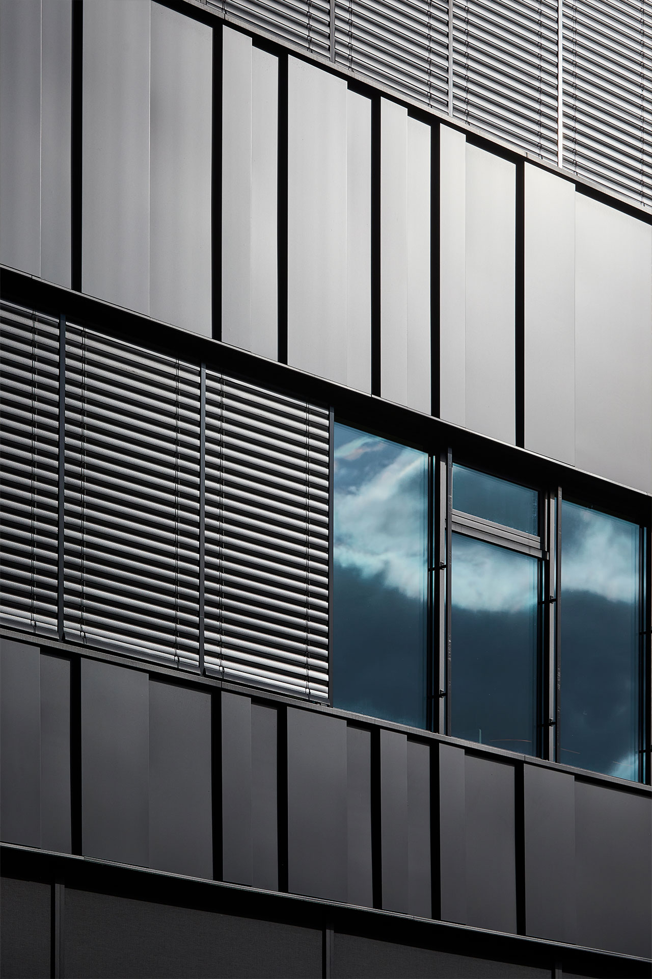 Modern building exterior with vertical metal panels and large glass windows reflecting the blue sky.