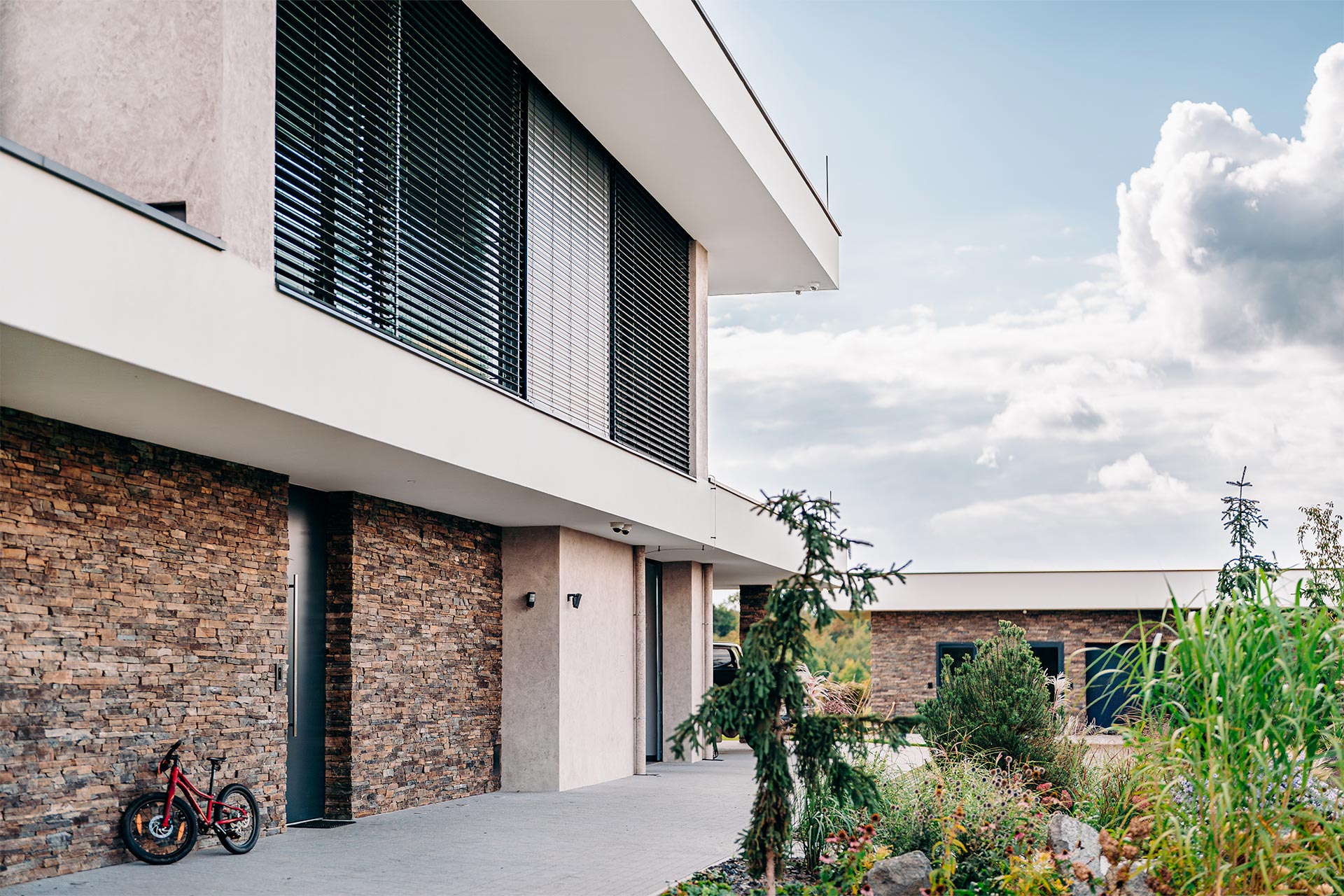 Modern building facade with stone cladding and large windows with blinds; a red bicycle rests against the wall.