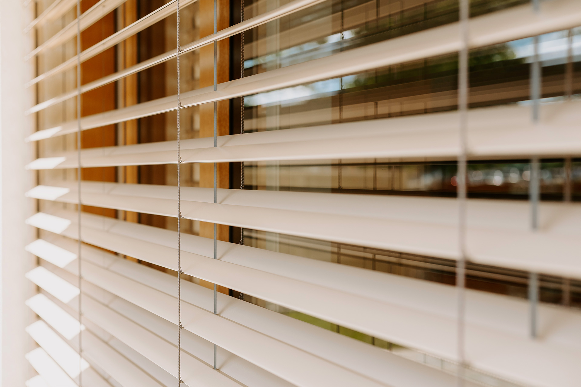 White horizontal blinds covering a window, cords hanging down, soft daylight filtering through.